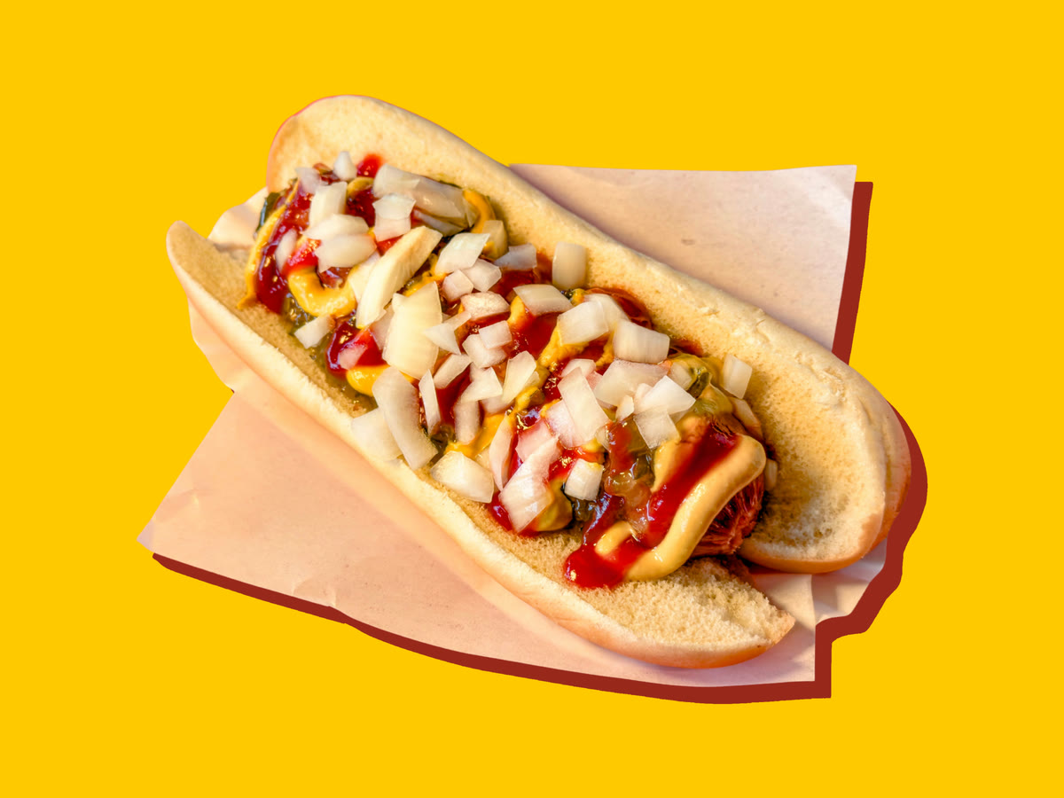 An all-beef hot dog in a bun, topped with diced onions, ketchup, mustard and relish, on deli paper