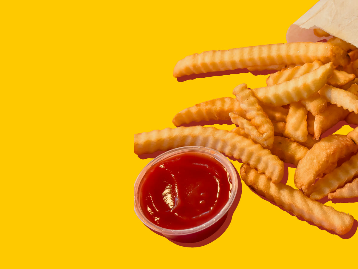 Crinkle-cut French fries spilling from a paper bag, beside a cup of ketchup