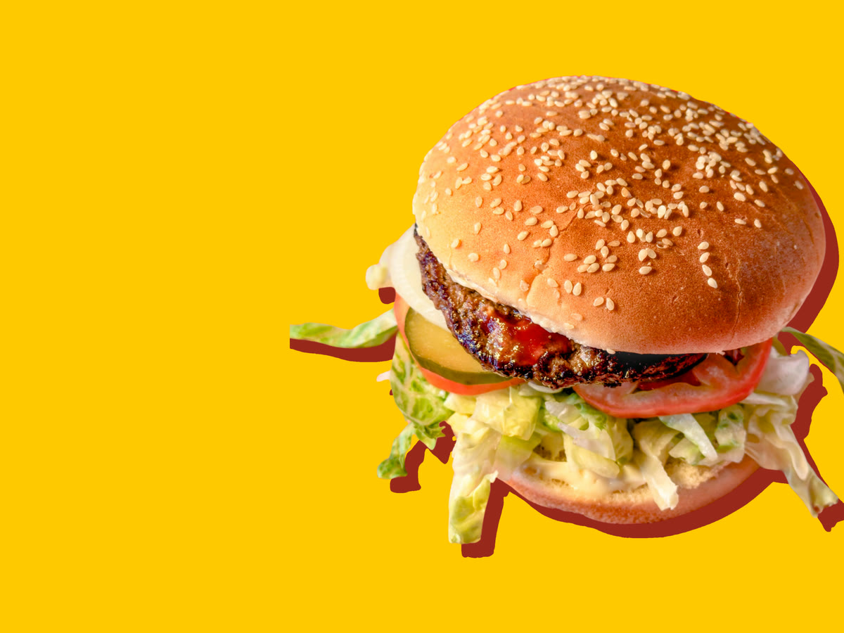 A beef burger on a sesame bun, with ketchup, onion, pickles, tomato and shredded lettuce with mayonnaise