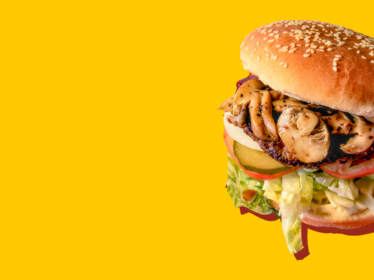 A sautéed mushroom burger on a sesame bun, with onion, a pickle, tomato and shredded lettuce