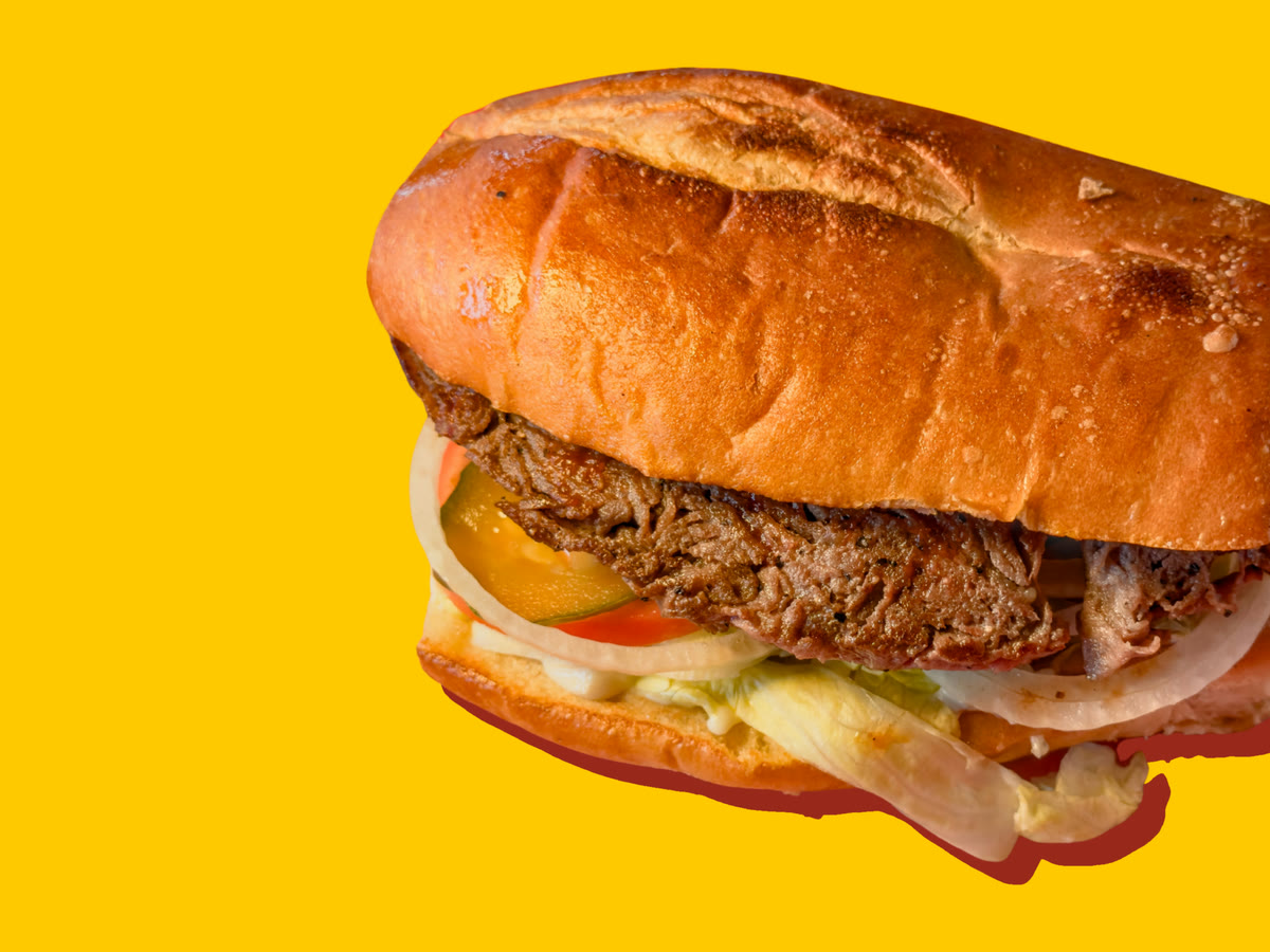A tender steak sandwich on a toasted French roll, with pickles, tomato, onion, shredded lettuce and mayonnaise