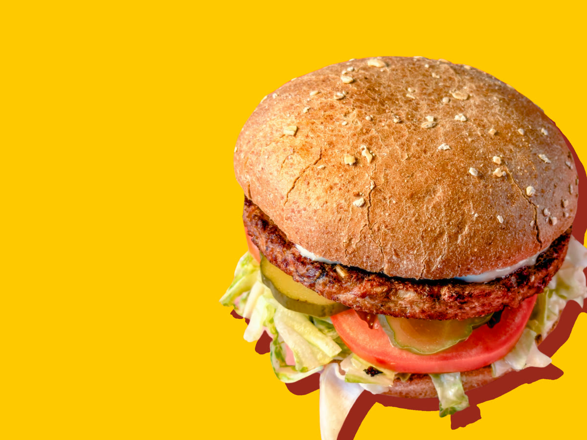 A vegetarian burger on an oat-topped wheat bun, with mayonnaise, pickles, a tomato slice and shredded lettuce